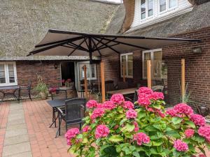 a patio with a black umbrella and pink flowers at Tetens Gasthof in Süderlügum