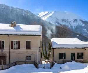 a house in the snow with mountains in the background at Casa Lola nel centro storico di Bolognola in Pintura di Bolognola