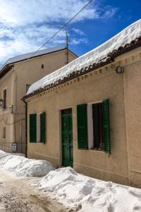 a building with green shutters and snow in front of it at Casa Lola nel centro storico di Bolognola in Pintura di Bolognola