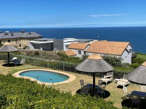 a swimming pool with chairs and umbrellas and the ocean at VIlla for Family and Golf in Mossel Bay