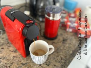a red coffee maker making a cup of coffee at Mediterrâneo 507 - Todo Equipado, Ar Condicionado, Churrasqueira na Varanda, Internet Fibra 600MB, Estacionamento Grátis in Cabo Frio