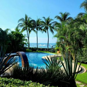 a swimming pool with palm trees and the ocean at The Inn Manzanillo Bay in Troncones