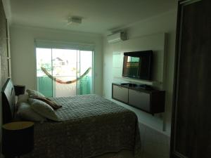 1 dormitorio con 1 cama, TV y ventana en Linda casa com piscina e 4 suites no mariscal a 100 metros da praia, en Bombinhas