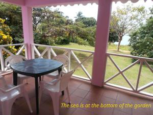 a porch with a table and chairs and a view of the garden at The Pink House in Choiseul