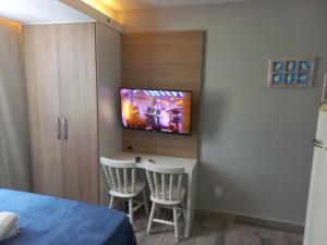 a bedroom with a tv on a wall with two chairs at Flat Beverly Hills 101B in Vila Velha