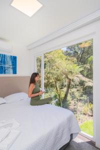 a woman sitting on a bed looking out a window at KŌN - Pousada Romântica in São Francisco de Paula