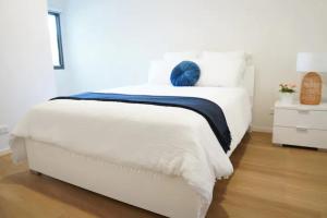 a white bed with a blue pillow on top of it at ViQi Two bedroom apartment front of century walk Including Premium NETFLIX & Prime AMAZON with 75 INCH TV in Glen Waverley