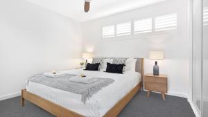 a white bedroom with a bed with two towels on it at Luxe by the Lake in Lake Illawarra