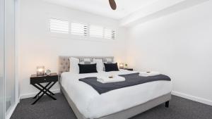 a white bedroom with a large bed with two towels on it at Luxe by the Lake in Lake Illawarra +37 photos