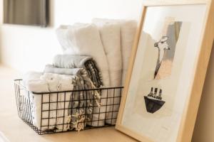 a basket of towels and a framed picture next to a mirror at Petit hôtel de la Montagne in Havre-Aubert