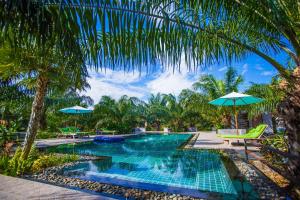 盼武里Palm Pran Resort的度假村内带椅子和遮阳伞的游泳池