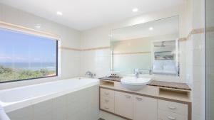 baño con bañera, lavabo y ventana en The Sands Resort at Yamba, en Yamba