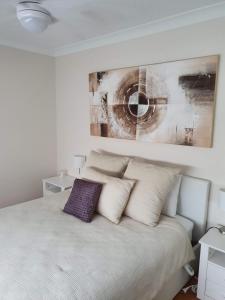 a bed with white pillows and a painting above it at House Beside The Lake in Summerland Point