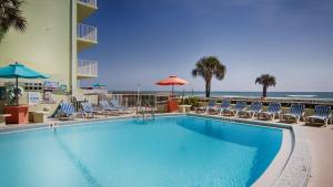 a swimming pool with chairs and umbrellas and the beach at El Caribe Resort and Conference Center in Daytona Beach