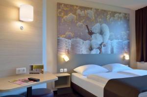 a hotel room with a bed and a desk and a painting at B&B Hotel Düsseldorf-Ratingen in Ratingen
