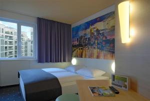 フランクフルト・アム・マインにあるB&B ホテル フランクフルト シティ-オストのベッド、デスク、窓が備わるホテルルームです。