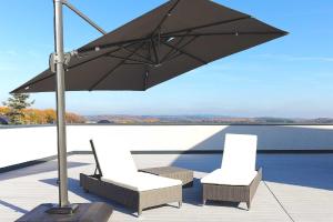 zwei Stühle und ein Regenschirm auf einer Terrasse neben dem Wasser in der Unterkunft Apartments Panoramablick in Mettlach