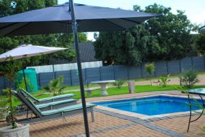 an umbrella and chairs next to a swimming pool at Tranquility Guesthouse in Standerton