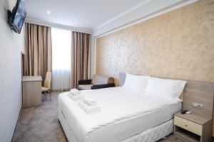 um quarto de hotel com uma cama branca e uma cadeira em Hotel CITY Sandanski em Sandanski