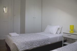 a white bedroom with two beds and a yellow vase at WW Hostel & Suites in Coimbra