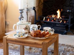 una mesa con tazas de té y comida y una chimenea en Swift Cottage en Blockley
