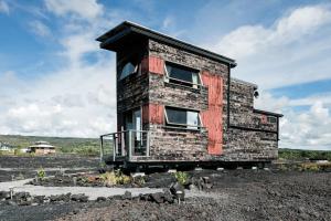 ein Backsteinhaus mit einem Balkon auf einem Feld in der Unterkunft THE PHOENIX HOUSE - EPIC Tiny Home Gem on Volcanic Lava Field! in Kehena