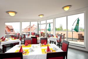 ein Restaurant mit weißen Tischen und roten Stühlen und Fenstern in der Unterkunft Müritzperle in Waren (Müritz)