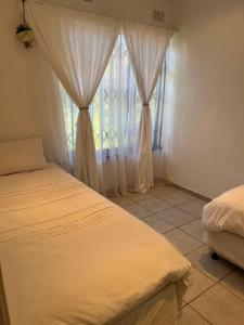 een slaapkamer met 2 bedden en een raam met gordijnen bij Mtunzi Park, 39 Peaceful shores in Scottburgh