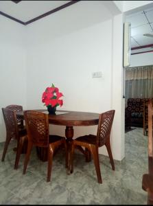 una mesa de madera con sillas y un jarrón con flores rojas en Cinnamon Villa Boossa, en Busse