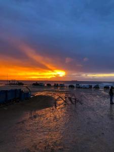 a sunset on a beach with people standing in the water at Appartement youssef in Agadir