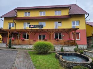 a yellow and red house with a pond in front of it at Penzion Adak in Párnica