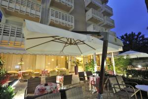 une terrasse avec un parasol blanc, des tables et des chaises dans l'établissement Hotel Eros, à Lignano Sabbiadoro