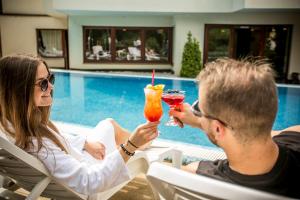 Een man en vrouw die in stoelen cocktails drinken bij het zwembad. bij Bassiana Hotel es Etterem in Sárvár