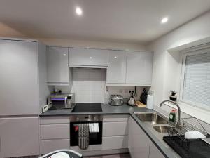 uma cozinha com armários brancos e electrodomésticos de aço inoxidável em New build home with WI-FI, Smart TV, dedicated office floor, large terrace and Free parking em Milton Keynes
