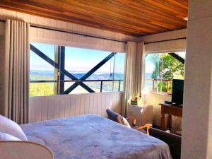 um quarto com uma cama e uma grande janela em Pousada Pedras e Sonhos em Monte Verde