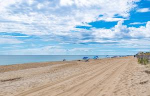 a sandy beach with people and umbrellas on it at Serendipity - KDH MP 6.5, Oceanfront, Amazing Ocean View, Hot Tub, Pets OK, YR Flex Stays in Kill Devil Hills