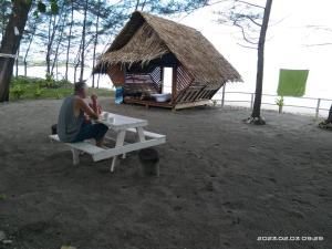 a man sitting on a picnic table in front of a hut at Tammoyo Place in Kudat