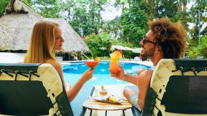 Ein Mann und eine Frau sitzen mit Getränken am Tisch in der Unterkunft Cariblue Beach and Jungle Resort in Puerto Viejo