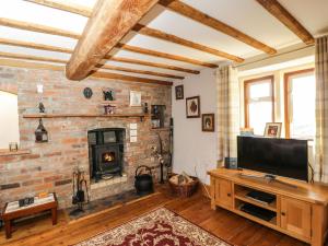 a living room with a brick fireplace and a television at Hen's Cottage in Chippenham