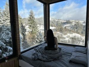 una mujer sentada en una cama mirando por una ventana en Forest Hub, en Slavske