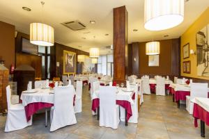 un restaurante con mesas y sillas blancas y lámparas de araña en Hostal Restaurante Alarico, en Allariz