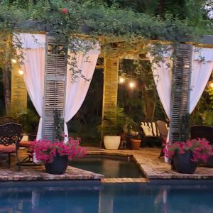 een patio met een zwembad en gordijnen en bloemen bij Cedar Oaks Inn The Bath House in Dickinson