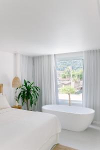 een witte slaapkamer met een bad en een groot raam bij Olisa Hotel Boutique in Maresias