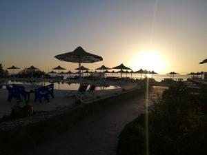 een strand met parasols, tafels en stoelen en de zonsondergang bij Silver Beach Boutique Hotel in Quseir