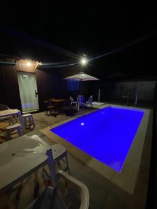 una piscina azul por la noche con mesa y sillas en Casa Rio da Madre, en Palhoça