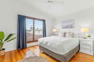 a white bedroom with a large bed and a window at Beach House in Lennox Head