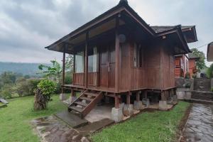 a wooden house with a porch on top of a yard at Kanaka Residence Mitra RedDoorz in Bandungan