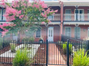 uma cerca em frente a uma casa com flores cor-de-rosa em Modern City Townhouse with all the Comforts em Wagga Wagga