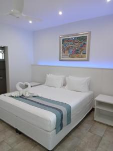 a bedroom with a white bed with a painting on the wall at Hotel La Roussette in Anse aux Pins