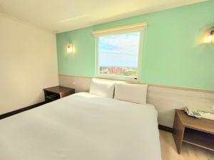 a bedroom with a large white bed and a window at Apple Hotel in Taitung City